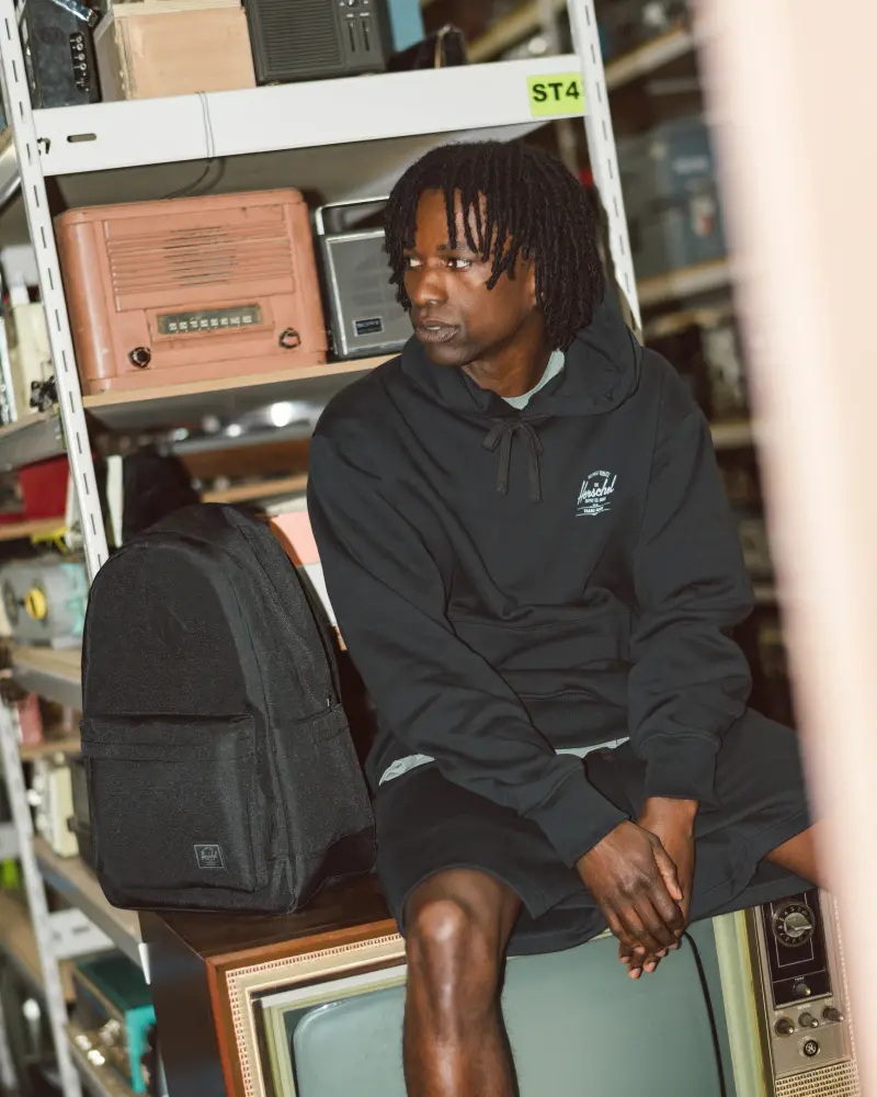 a man in a black classic hoodie sits on top of an old CRT tv