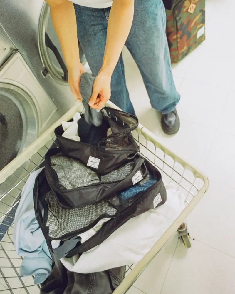 a pile of full kyoto packing cubes sit in a cart at a laundromat