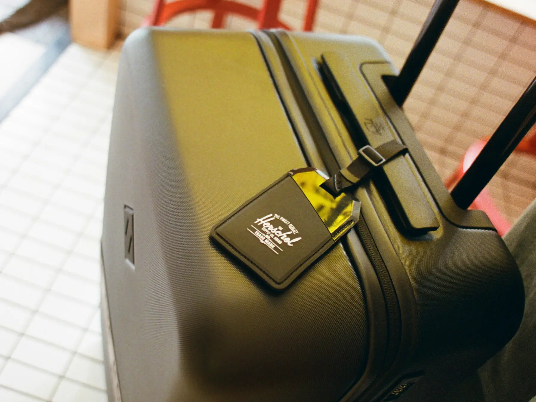 A close up photograph of a large black herschel heritage hardshell luggage with a luggage tag hanging over the zipper showing the herschel classic logo.